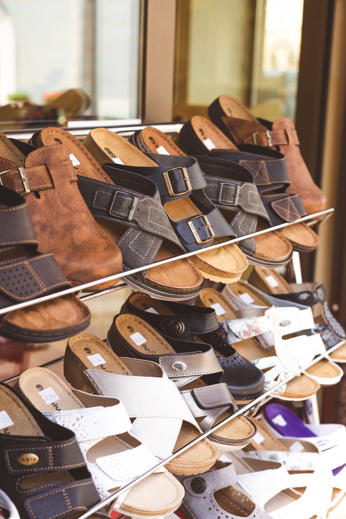 services-03 Close-up of leather sandals on shelves in a shoe store, showcasing different styles and colors.