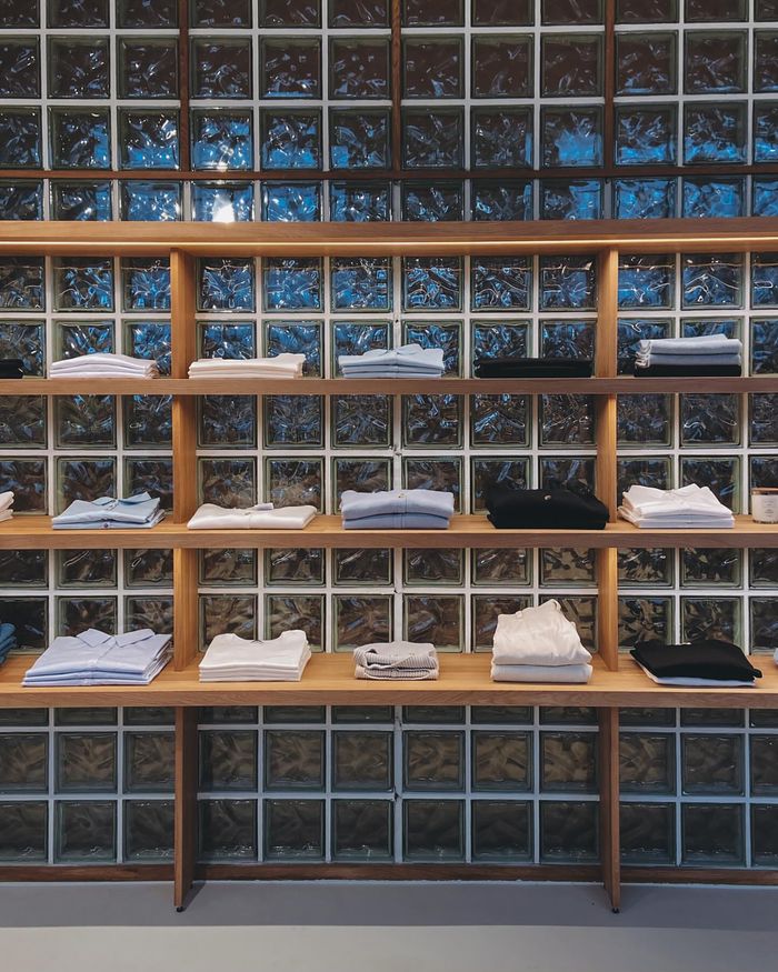 services-02 Organized display of folded shirts on wooden shelves against a glass block wall.