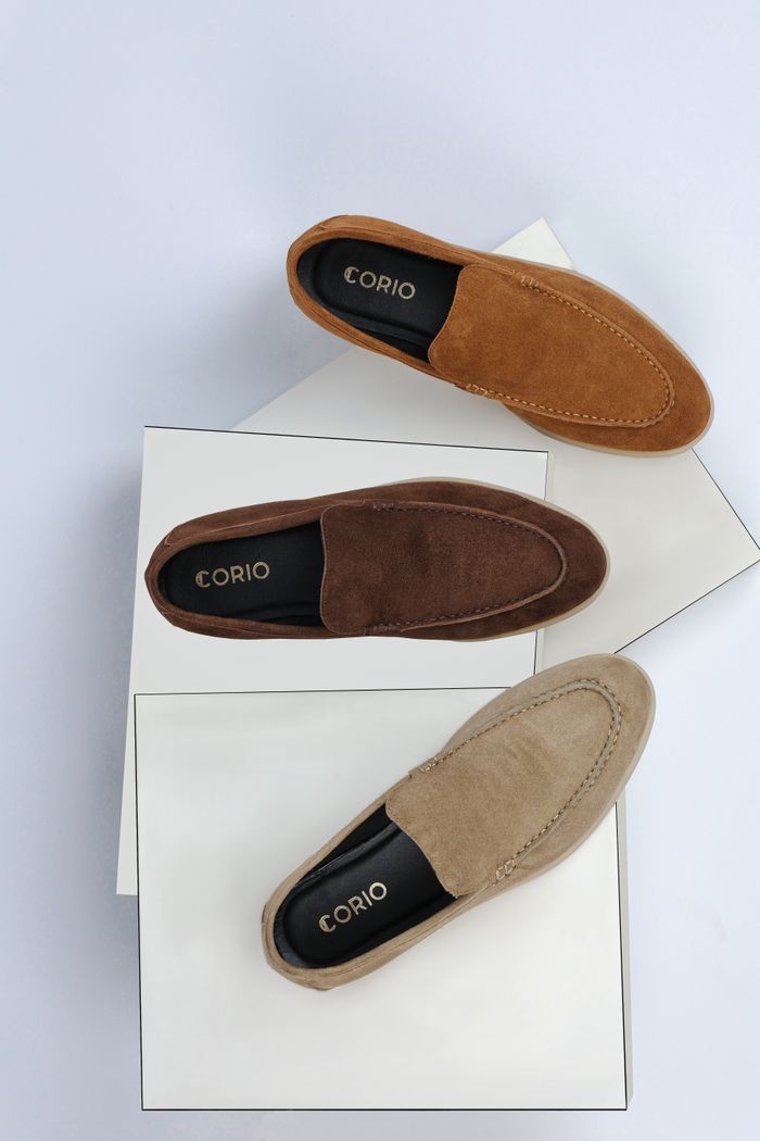Elegant suede loafers in various colors displayed on white boxes from above.
