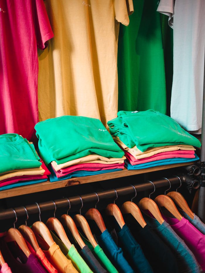 hero-img-02 Vibrant and neatly organized closet with colorful t-shirts folded and hanging.